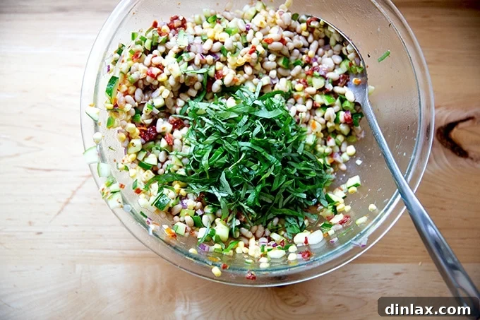 Freshly chopped basil leaves being added to a large bowl of tossed white bean salad.