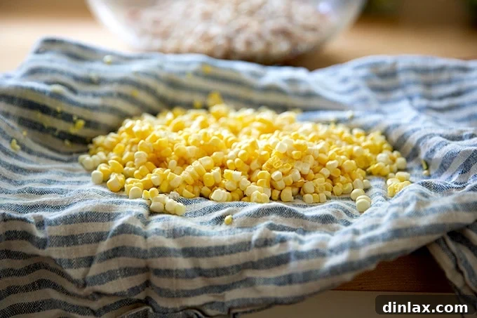 Fresh corn kernels neatly gathered in a striped tea towel on a countertop, after being stripped from the cob.