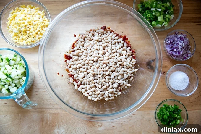 All the vibrant ingredients for the bean salad, including beans, corn, zucchini, red onion, and jalapeño, gathered on a countertop ready for mixing.