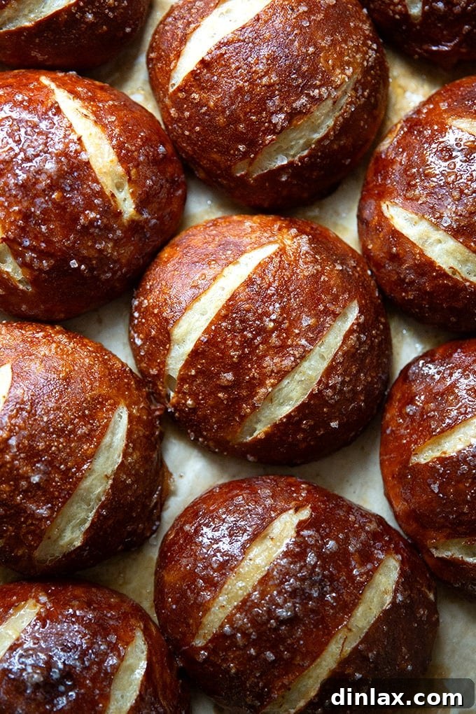 Freshly baked golden-brown pretzel rolls cooling on a parchment-lined sheet pan.