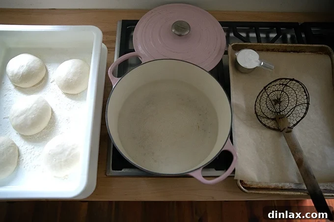 A pot of water heating on the stove, alongside proofed pretzel roll dough and a sheet pan.