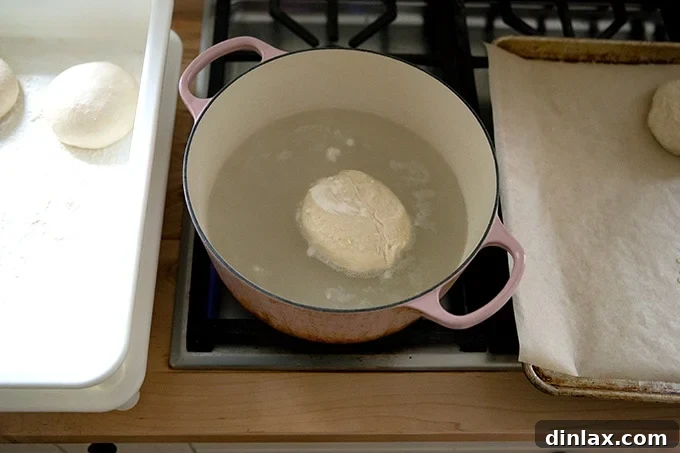 A pretzel roll briefly floating in a pot of simmering baking soda water.