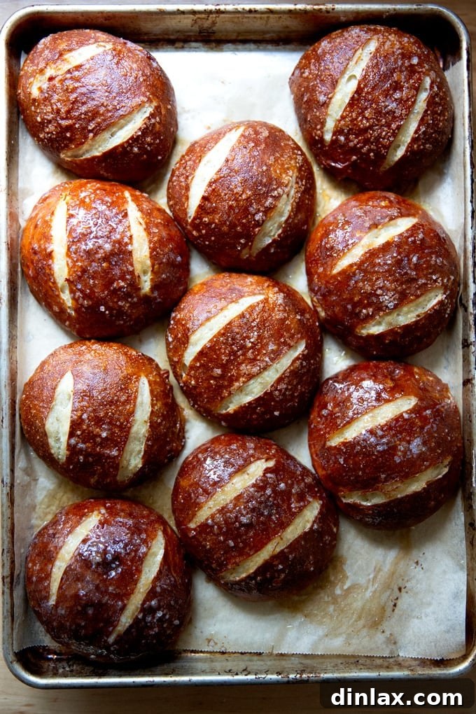 Just-baked pretzel rolls on a sheet pan, being brushed with melted butter.