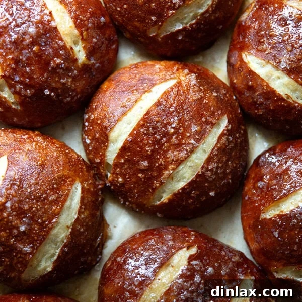Freshly baked golden-brown pretzel rolls cooling on a parchment-lined sheet pan.