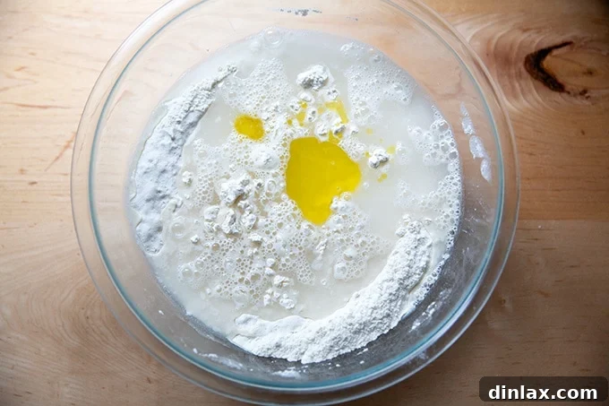 Water and olive oil being poured into the bowl of dry ingredients for pretzel roll dough.