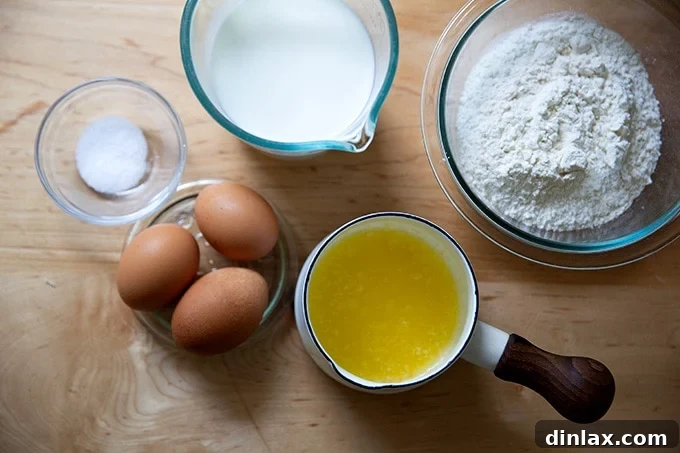 Various ingredients like eggs, milk, flour, and butter laid out on a counter to make popovers.