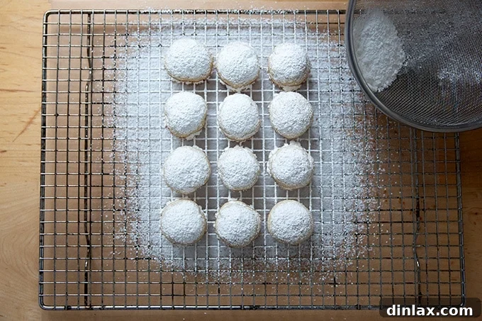 Warm lemon-almond snowball cookies arranged on a wire cooling rack, gently dusted with a pristine layer of powdered sugar.