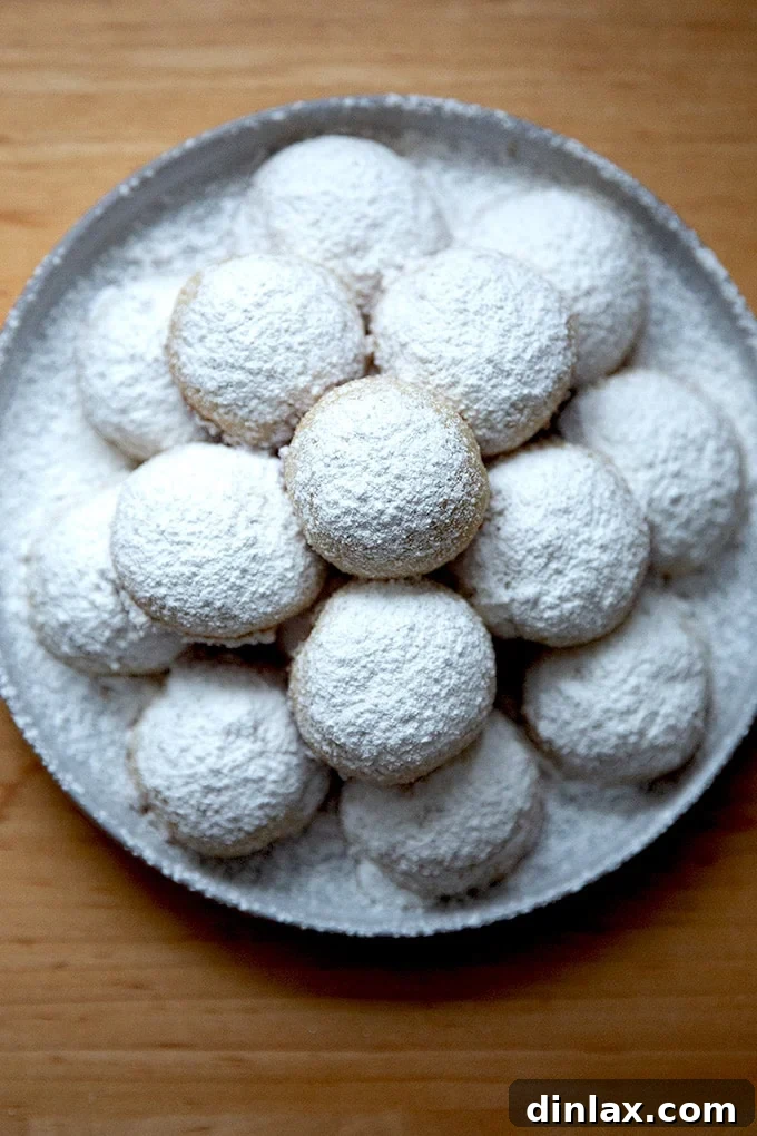A delightful plate brimming with lemon-almond snowball cookies, perfectly round and generously powdered, inviting immediate enjoyment.
