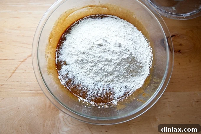 Perfectly Imperfect Gingerbread Cookie Bars 10 All-purpose flour being gently added to the spiced wet mixture in a large bowl, ready for final incorporation into dough.