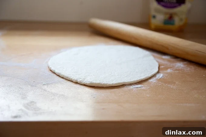 A gluten-free pizza crust being gently rolled out on a countertop.