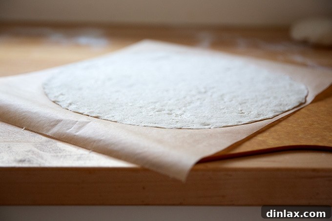 Rolled out gluten-free pizza dough placed on a parchment-lined pizza peel, with edges pinched.