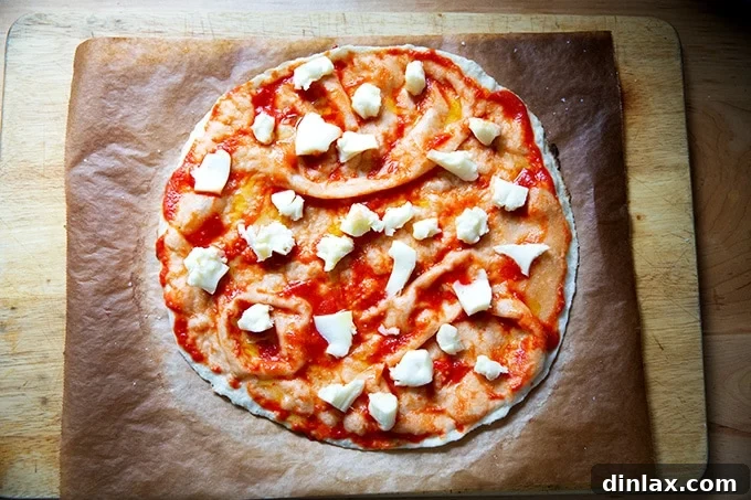 A gluten-free Margherita pizza, fully topped with sauce, mozzarella, olive oil, and salt, ready for its final bake.