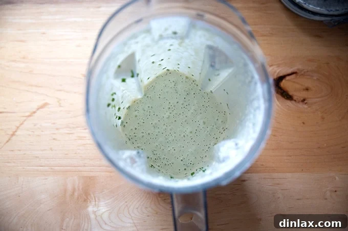 The finished vegan ranch dressing, perfectly blended with chives, visible as green flecks throughout the creamy mixture in the Vitamix.