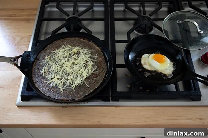 Light and Delicate Gluten Free Buckwheat Crepes 18 Two skillets on a stovetop: one containing a fried egg cooking, and the other holding a buckwheat crepe topped with melting grated cheese.