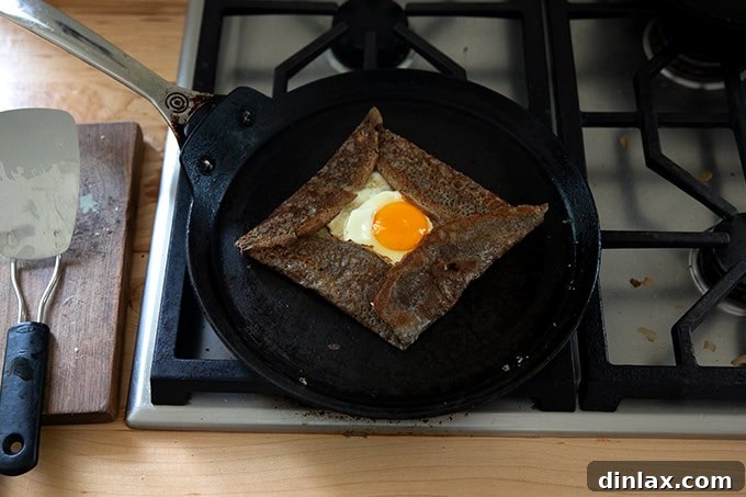 Light and Delicate Gluten Free Buckwheat Crepes 20 A skilled hand carefully folding the edges of the buckwheat crepe inwards, forming a neat square around the egg and melted Gruyere cheese filling within the skillet.