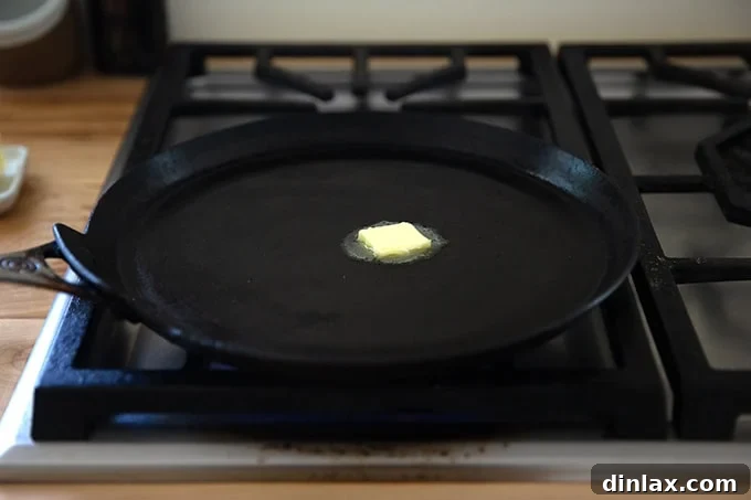 Light and Delicate Gluten Free Buckwheat Crepes 9 A nonstick crepe pan sitting on a stovetop burner, with a small pat of butter melting in its center, preparing for the first crepe.
