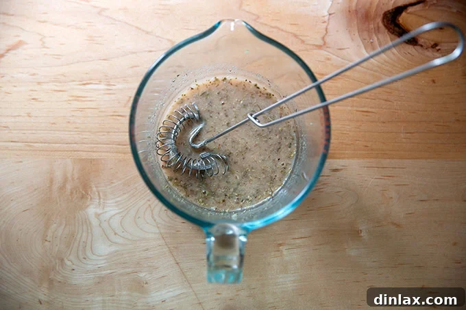 A liquid measuring cup containing a well-whisked mixture of red wine vinegar, lemon juice, salt, sugar, mustard, garlic, and oregano.