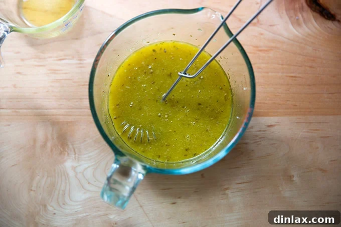 The complete Italian dressing, with olive oil streamed in and fully emulsified with the other ingredients, creating a smooth mixture in a liquid measuring cup.