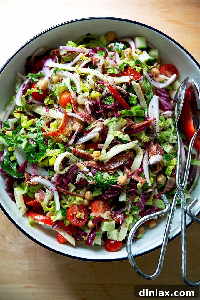 A large, inviting salad bowl overflowing with a classic chopped salad, tossed with Italian dressing and ready to serve with tongs.