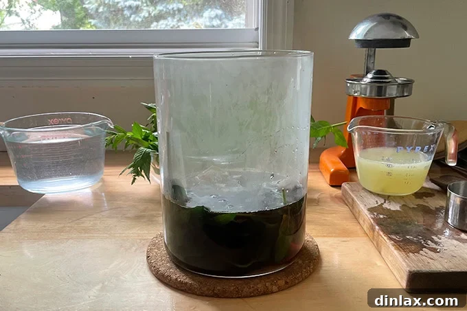 A hand reaching into a glass vessel to remove tea bags and mint after steeping in hot water, with the tea's color visible.