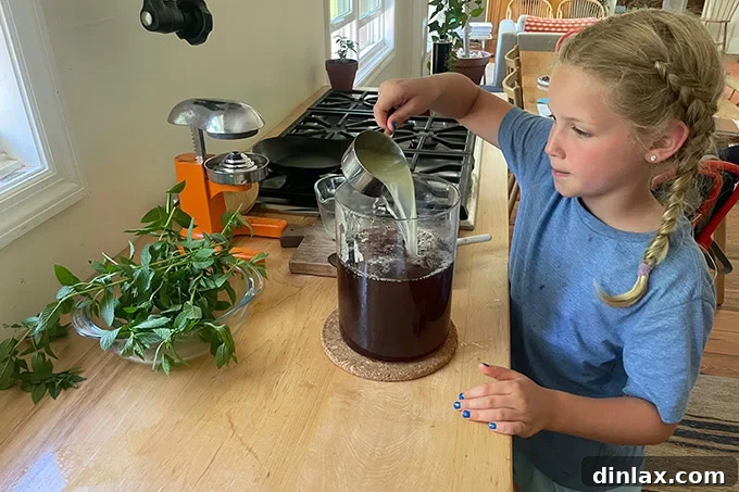 A young girl, Tig, carefully pouring fresh lemon juice into a large pitcher of brewed tea, adding the final flavor component.
