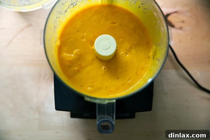 Pureed yellow tomato sauce in a food processor, now beautifully smooth and vibrant after the final blending with butter, ready for tasting and seasoning adjustments.