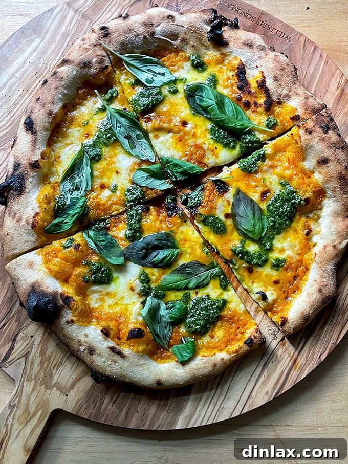 A delectable homemade pizza featuring a base of golden yellow tomato sauce, adorned with fresh basil pesto swirls and bright green basil leaves, offering a unique and flavorful twist.