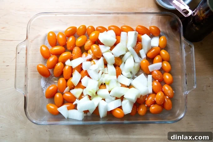 A large 9x13-inch baking pan, generously filled with glistening yellow cherry tomatoes and neatly chopped onions, perfectly coated with olive oil and salt, awaiting roasting.