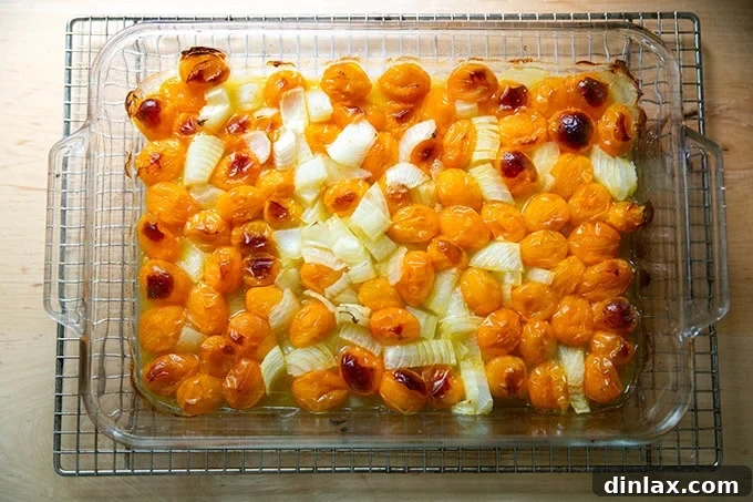 A baking pan filled with roasted yellow cherry tomatoes and onions, their skins perfectly blistered and softened, indicating they are ready for the next step of sauce preparation.