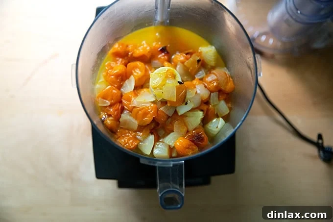 A food processor filled to the brim with fragrant roasted yellow tomatoes and onions, ready to be blended into a smooth and delicious sauce.