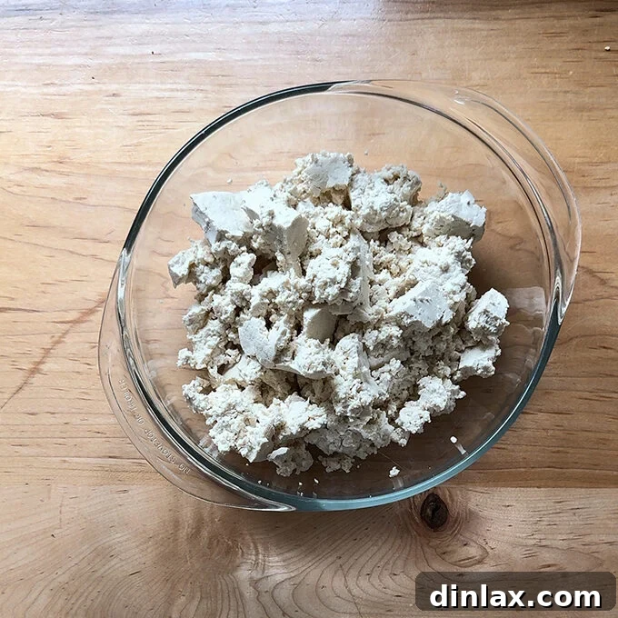 A bowl filled with hand-crumbled pieces of extra-firm tofu, showcasing its irregular, textured form.