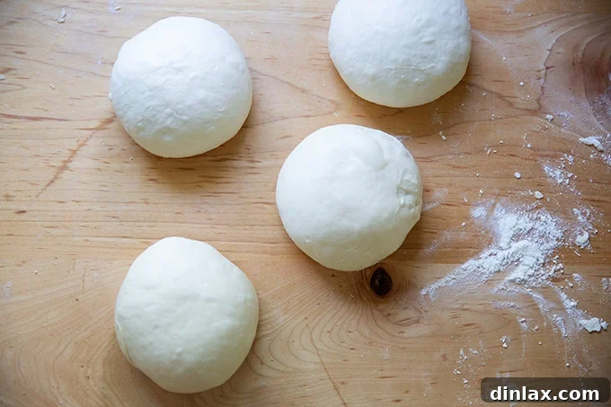 Four perfectly balled-up portions of baguette dough, smooth and taut.