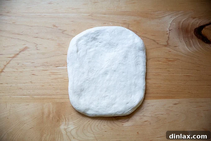 A flattened round of baguette dough, now shaped into a rough rectangle.