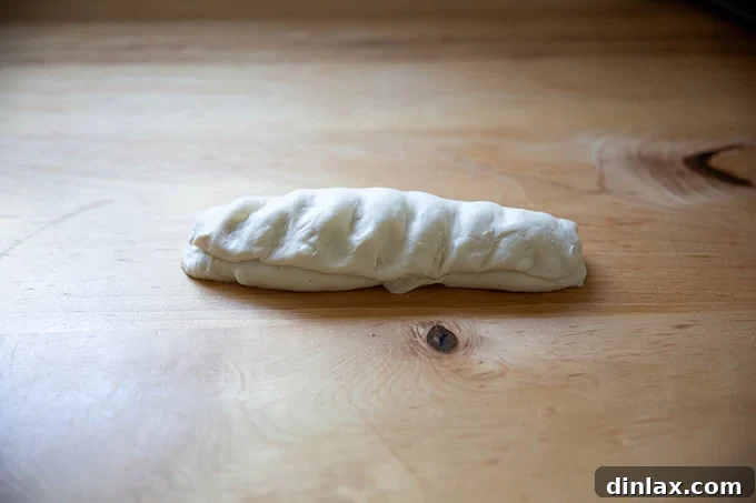 An unbaked baguette in the process of being shaped, with another fold applied from the top.
