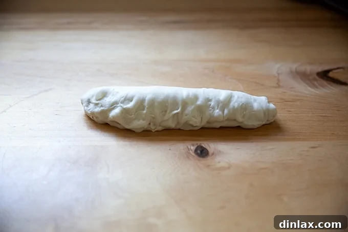 The final step of shaping an unbaked baguette, with the seam being pinched tightly to seal it.