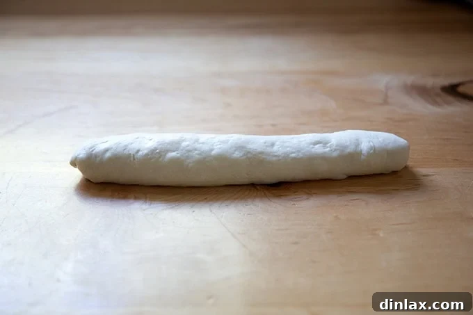 A beautifully shaped unbaked baguette, smooth and elongated, resting on a surface.