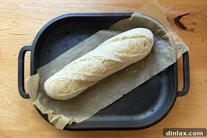 A partially baked baguette, golden and risen, visible inside an uncovered Challenger Bread Pan.