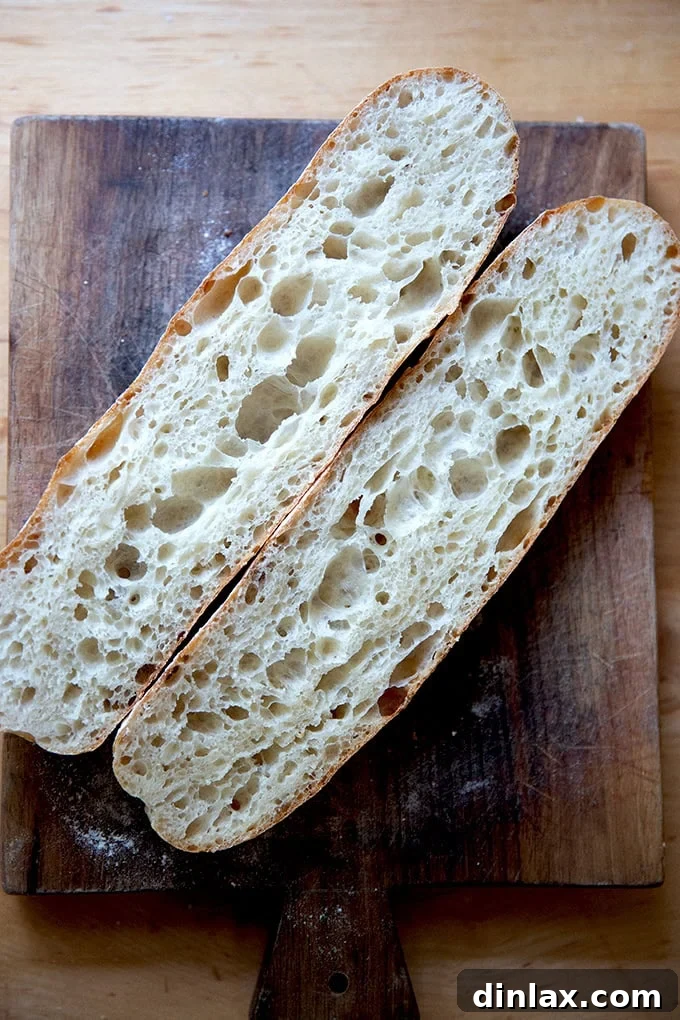 One freshly baked baguette, halved lengthwise, revealing its airy, open crumb on a cutting board.