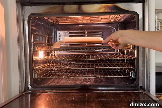 A baguette being carefully slid onto a preheated Baking Steel inside an oven using a pizza peel.