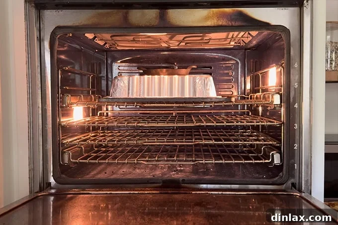 A disposable aluminum pan inverted over a baguette on a baking steel, weighted down to trap steam.