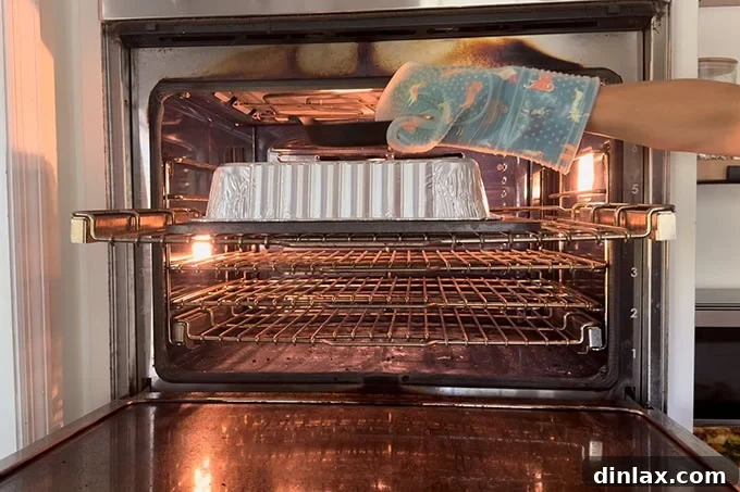 A hand removing a heavy weight from an aluminum pan covering a baguette on a baking steel in the oven.