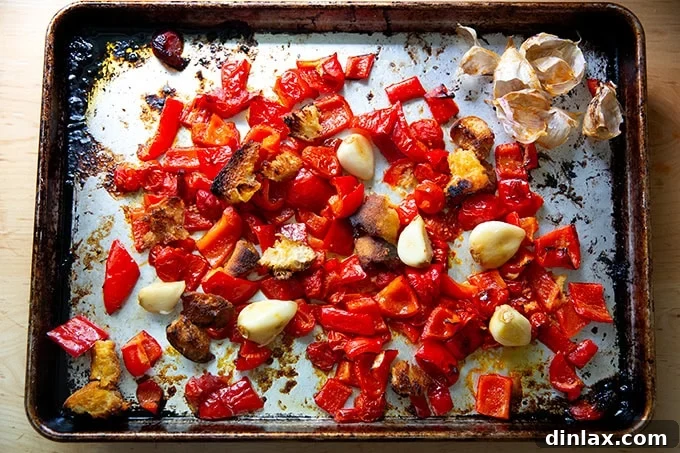 Zahmetsiz Romesco Sosu: Biberleri Soymaya Son! 8 Peeled garlic cloves among other roasted vegetables to make romesco sauce on a sheet pan.