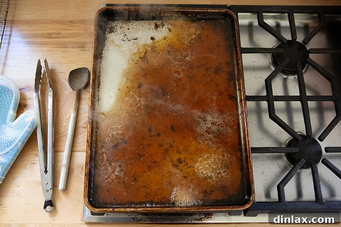 Make Ahead Roasted Turkey Wing Stock 11 A sheet pan positioned across two stovetop burners, with 2 cups of water added, initiating the deglazing process to capture rich fond.