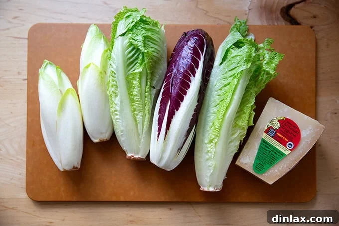 Perfect Caesar Dressing Your Way 13 Various types of fresh lettuce and a wedge of Parmigiano Reggiano cheese displayed on a wooden cutting board.