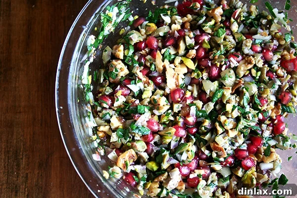 A vibrant bowl of green olive, walnut, and pomegranate salad, garnished and ready for a holiday feast.
