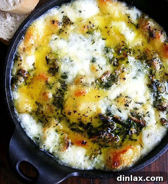 Baked fontina with rosemary and thyme in a cast iron skillet, hot and bubbly from the oven, garnished with fresh herbs.