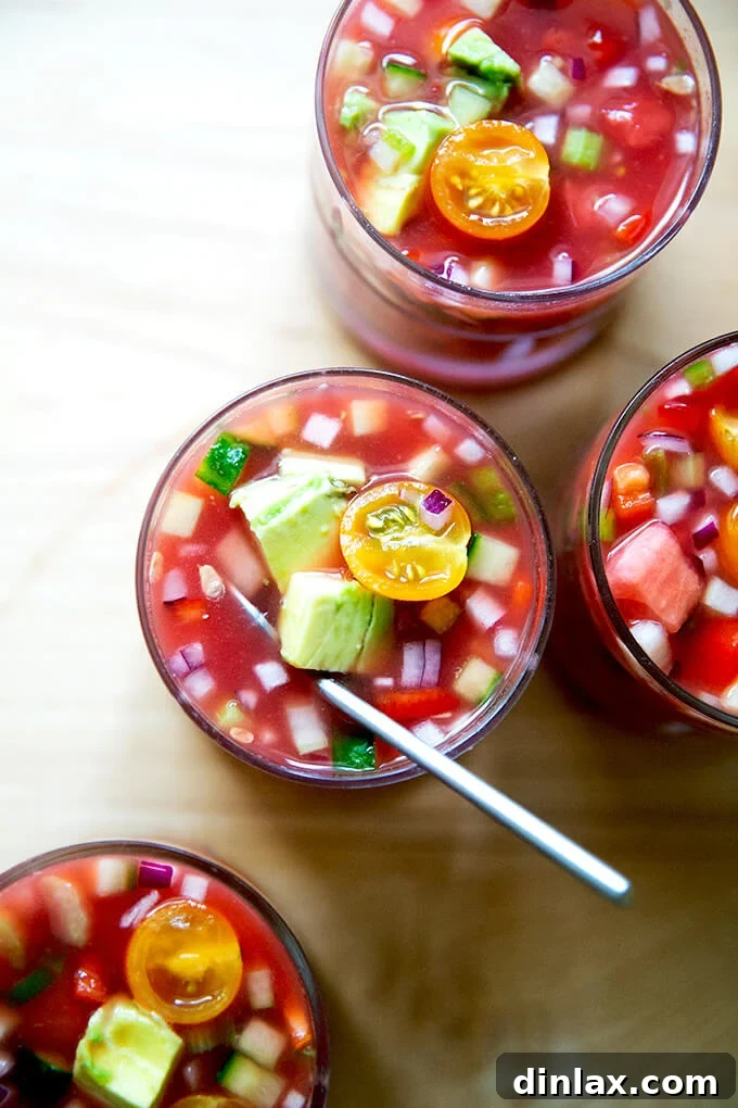 Several small, clear glasses individually portioned with watermelon gazpacho, garnished with avocado.