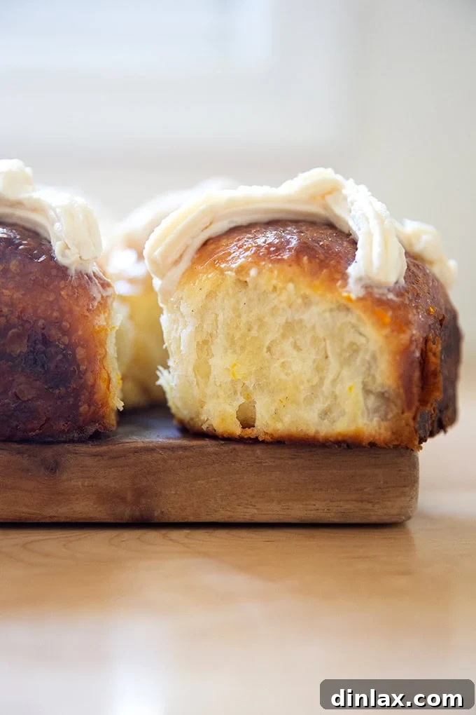 A close-up side view of a freshly baked hot cross bun, showcasing its tender texture and classic white cross design.