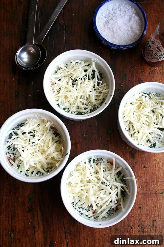 4 ramekins each holding an egg, cheese and herbs, ready for the oven.