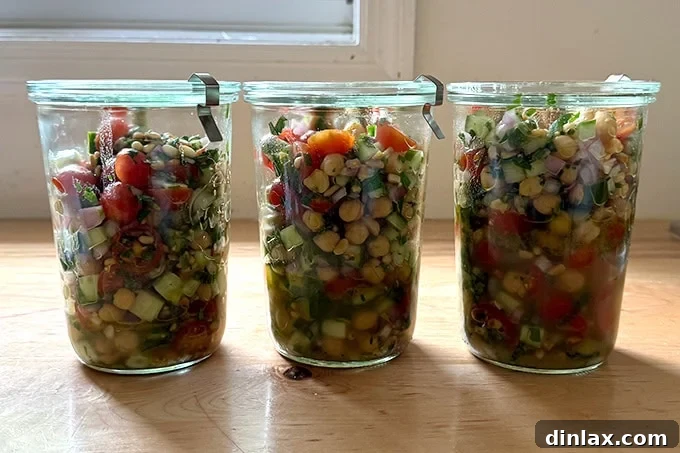Portions of the herby chickpea salad neatly packed into glass storage jars, illustrating its convenience for meal prepping and refrigerated storage.